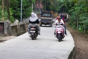 Warga mengendarai sepeda motor dan mobil pikap di jalan desa yang sudah dibeton mulus
