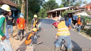 Pekerja berompi oren meratakan semen cor rigid jalan lingkungan poros kampung di Pandeglang