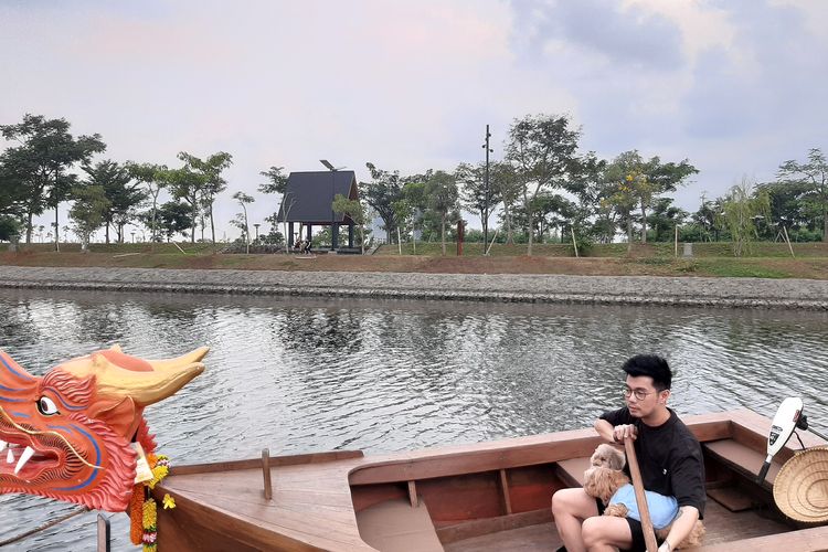 Pengunjung pria mengayuh perahu kayu berhias kepala naga bersama hewan peliharaan anjing di aliran Sungai Tahang Greenbelt PIK 2 Tangerang.